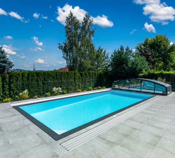 Létó u bazénu: děti si hrají ve vodě, dospělí odpočívají, pes a žena