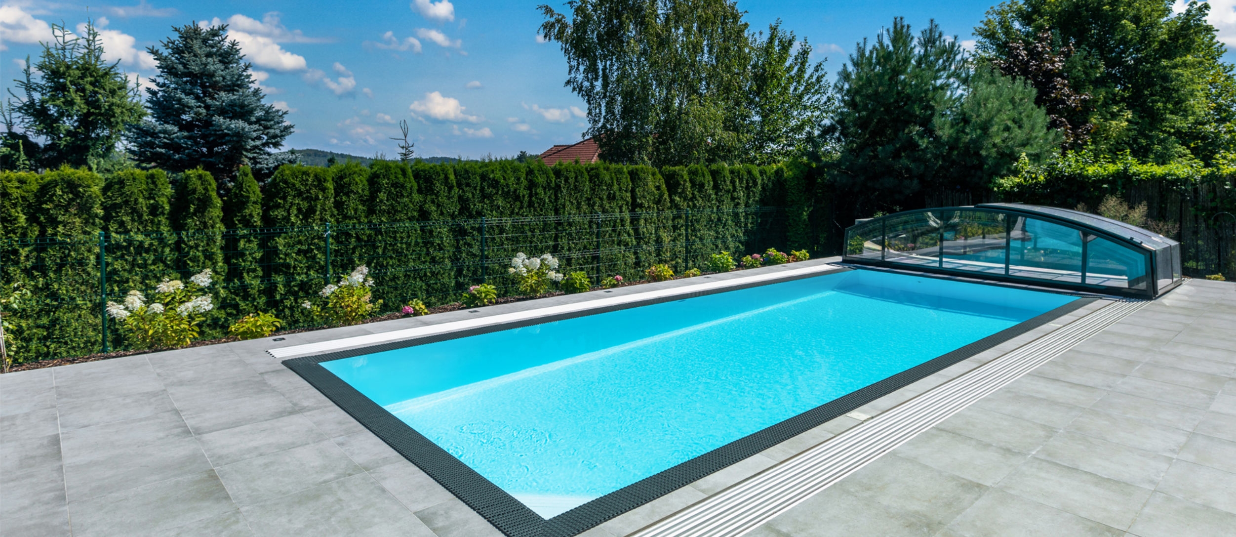 Létó u bazénu: děti si hrají ve vodě, dospělí odpočívají, pes a žena